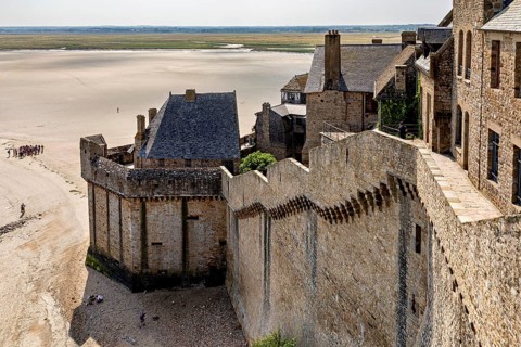 Historic castle wall with a view of a wide expanse of sand and distant buildings under a clear sky,
