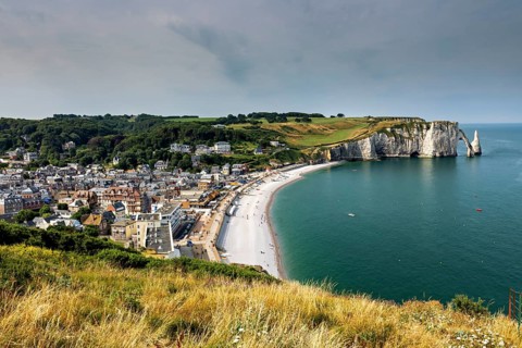 Coastal town with a bay surrounded by green hills, a lively beach promenade and clear water, The
