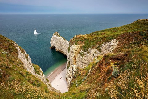 Green cliffs with sailing boat in the sea and small beach bay, The cliffs and alabaster coast of