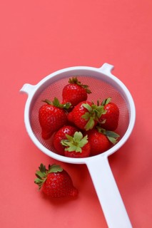 Strawberries in a colander on a red background, Fragaria