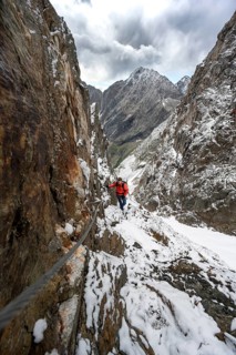 Mountaineer on a rope-secured path in a steep rocky mountain landscape with fresh snow in summer,
