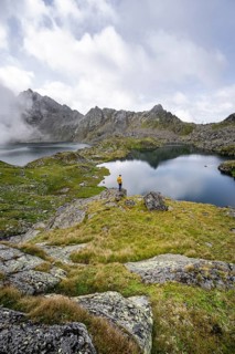 Mountaineer on a rock in front of mountain lakes Wangenitzsee and Kreuzsee, cloudy mountain peaks