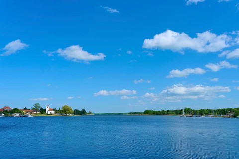 Lake with blue sky and clouds, in the background a village with a church, Rhodes, Etang du Stock,