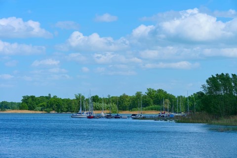 Lake with boats on the shore, surrounded by trees under a blue sky, Rhodes, Etang du Stock,