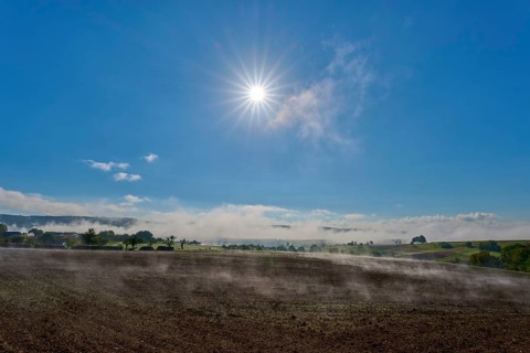 The sun shines brightly over a misty landscape stretching across wide fields, Mönchberg,