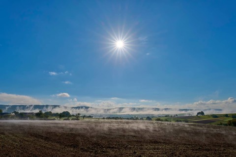 Under a clear sky, the sun shines over a misty, wide landscape, Mönchberg, Miltenberg, Spessart,