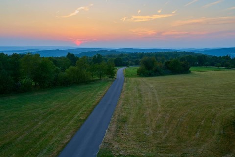 Narrow road winds through fields at sunset with orange sky, Geishöhe, Dammbach, Spessart, Bavaria,