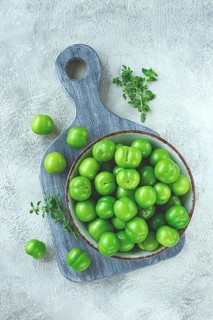 Tkemali, green cherry plum, in a bowl, on a gray table, top view, natural light, no people