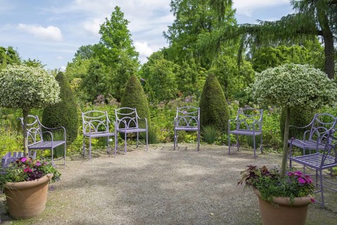 Purple garden chairs surrounded by green nature with trees and plants under a blue sky,