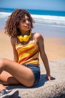 Young woman wearing headphones sitting on a rock at the beach, enjoying music and looking out at