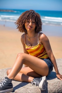 Young woman with curly hair sitting on a beach wall, enjoying the sunny weather and ocean view
