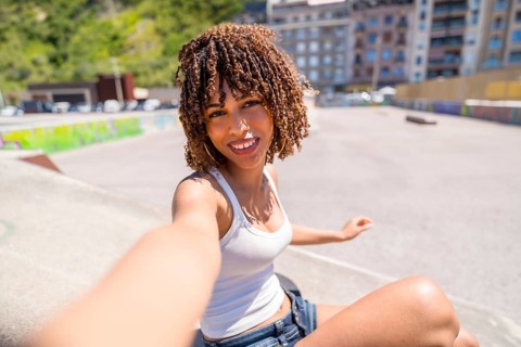 Smiling young woman with curly hair enjoying a sunny day at a skate park while taking a selfie