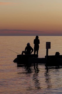 Silhouette of young adults ignoring danger sign while fishing on storm drain culvert in Long Beach,
