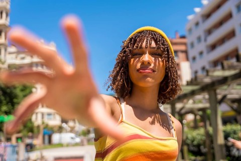 Stylish young woman extending her hand towards the camera in a vibrant city setting, enjoying a