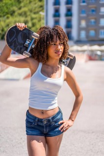 Confident young woman holding skateboard on shoulder, enjoying urban lifestyle and skateboarding