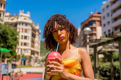 Fashionable young woman enjoys a cold beverage in a vibrant urban setting, embracing the summer