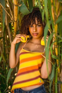 Young woman holding vibrant yellow headphones while posing gracefully in a lush bamboo forest,