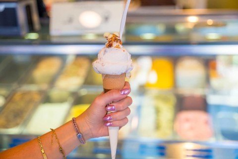Woman enjoying a delicious ice cream cone with toppings, inside a gelateria with a display case