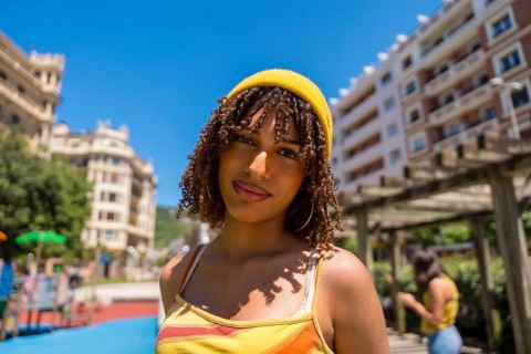 Portrait of a fashionable young woman with curly hair and yellow beanie enjoying a sunny day in an