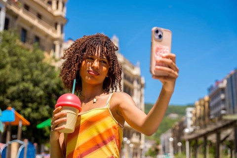 Stylish young woman captures a selfie while holding a refreshing beverage, enjoying a sunny day in