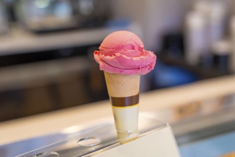 Refreshing pink ice cream scoop melting on crispy cone, displayed on showcase in ice cream shop,