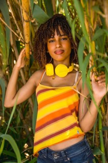 Young woman wearing yellow headphones, posing amidst vibrant bamboo trees, enjoying the soothing