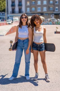 Two young women skaters posing with their skateboards at a vibrant skate park, enjoying the sunny