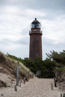 Path through sand dunes leads to the Darßer Ort lighthouse, surrounded by nature and cloudy skies,