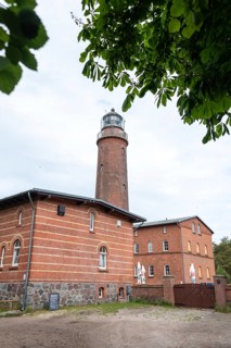 Lighthouse Darßer Ort, brick lighthouse next to a historic building, surrounded by trees under a