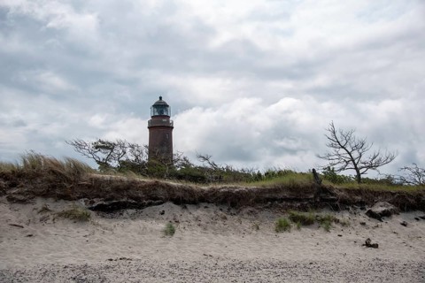Lighthouse behind sand dune with sparse vegetation and dramatic cloudy sky, Prerow,