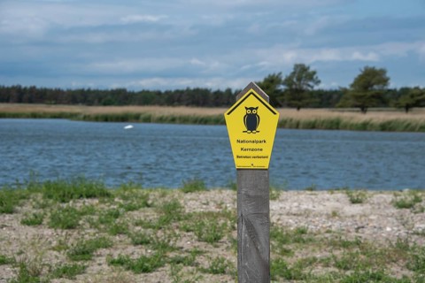 Yellow national park sign with owl in the foreground, water and cloudy sky in the background,