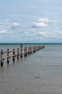 Wooden footbridge leads into the calm, blue sea under a slightly cloudy sky, Prerow,
