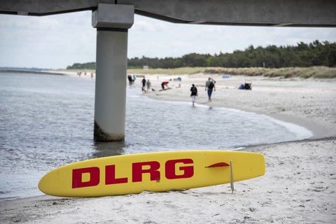 Yellow rescue board with red DLRG print on the beach under the bridge pillar, Prerow,
