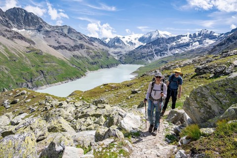 Mountaineer on a hiking trail at a blue mountain lake, reservoir Lac des Dix, behind mountain peak