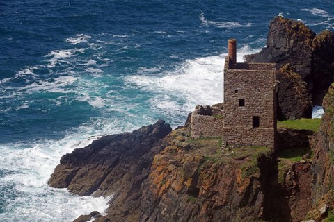 An old stone house perched on cliffs above a stormy sea with crashing waves, engine room, mining,