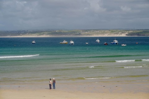 Boats anchored on calm waters off a wide, deserted sandy beach, St Ives, Cornwall, England, United