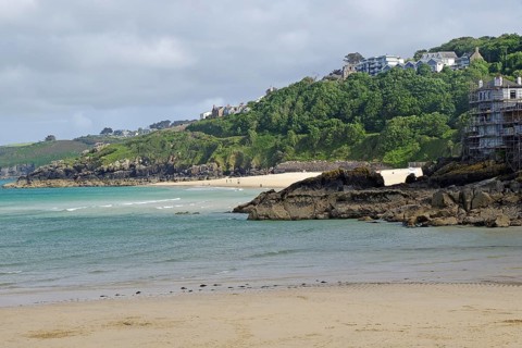 Sandy beach beach with sea view and hills covered with green trees and scattered houses, St Ives,