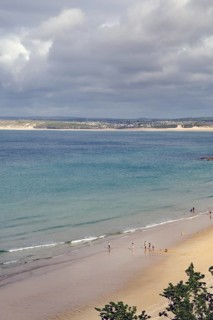 Several people walking on a quiet sandy beach, the sea under a cloudy sky, St Ives, Cornwall,