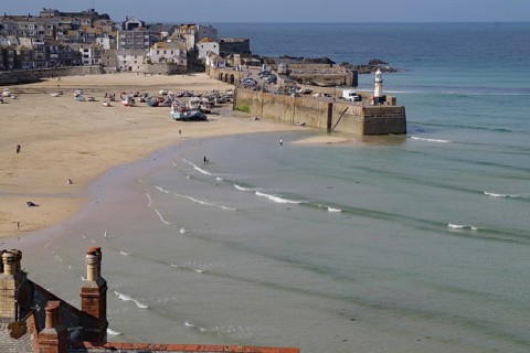 Coastal town with harbour and lighthouse, boats on the beach and gentle waves in the blue sea,