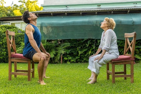 Senior woman and personal trainer engaging in seated exercises on chairs in a serene garden,