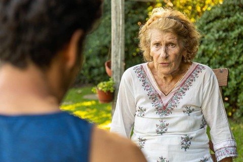 Elderly woman sitting comfortably on a wooden chair in a garden, engaging in a heartfelt