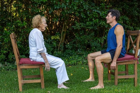 Senior woman and her personal trainer practicing rehabilitation exercises sitting on chairs in a