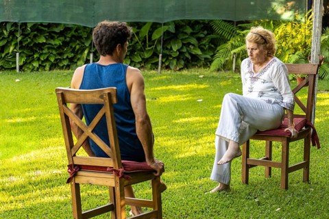 Senior woman and her physiotherapist are sitting on chairs in a garden, practicing rehabilitation