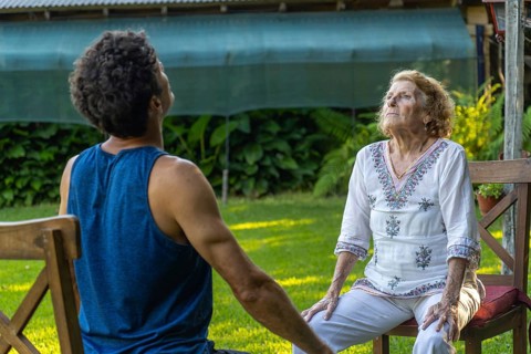 Senior woman and her physiotherapist are sitting on chairs in a garden, practicing breathing