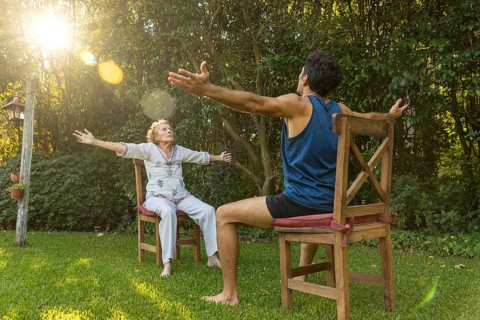 Senior woman practicing seated exercises with the assistance of a physiotherapist in a green