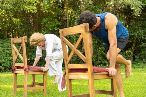 Senior woman and her personal trainer practicing a fitness routine using chairs as support in a