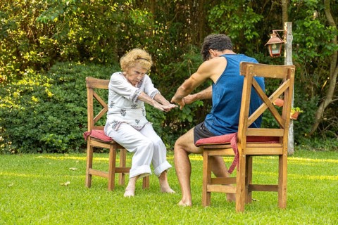 Elderly woman practicing physiotherapy with a personal trainer, performing exercises while sitting