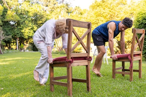 Senior woman and her physiotherapist are performing a rehabilitation exercise using chairs in a