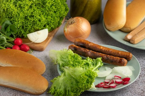 A plate with lettuce, onion, radish and sausage surrounded by bread rolls and ingredients