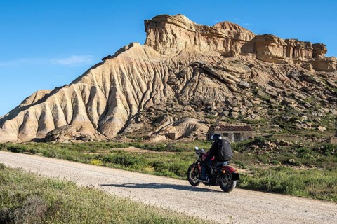 Biker riding motorcycle, gravel road, colorful rock formation, semi-desert, Bardena Blanca area,